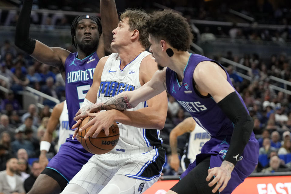 Orlando Magic center Moritz Wagner, center, tries to get off a shot as Charlotte Hornets center Mark Williams, left, and guard LaMelo Ball, right, defend during the first half of an NBA basketball game, Sunday, Nov. 26, 2023, in Orlando, Fla. (AP Photo/John Raoux)
