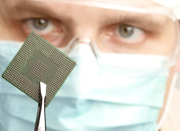 Technician using tweezers to hold up a semiconductor chip.