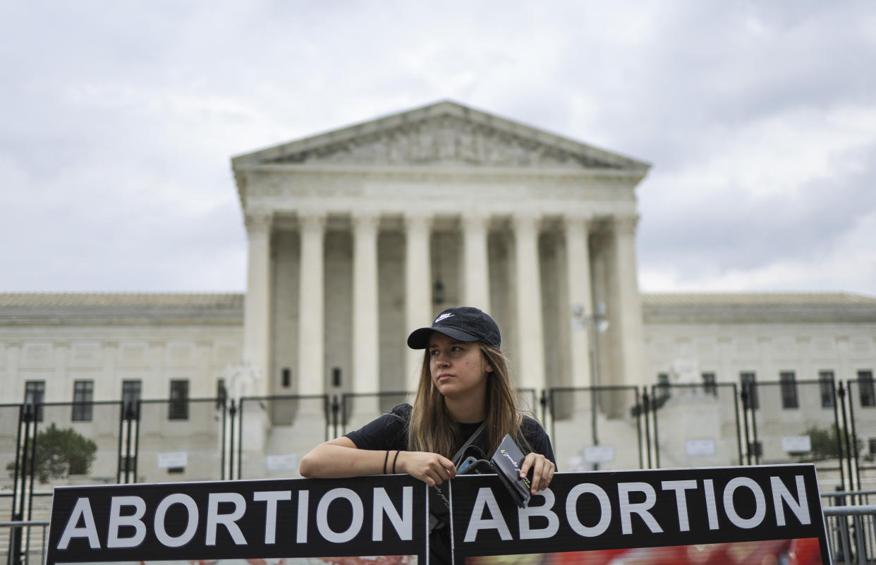 An anti-abortion activist props up two signs saying, in part, Abortion, outside the Supreme Court.