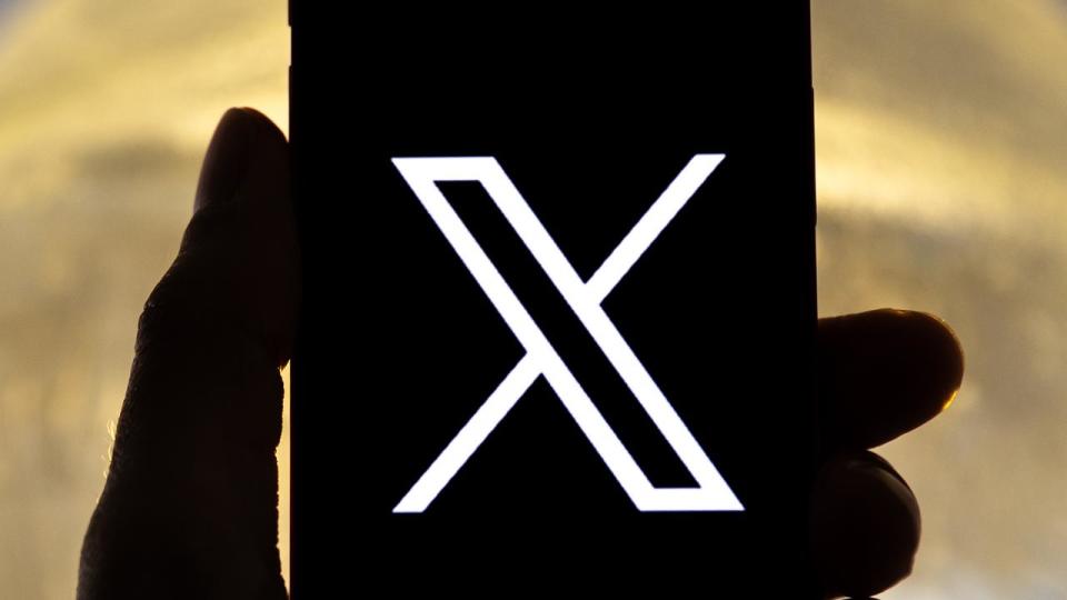 A user holding a mobile phone displaying the 'X' logo