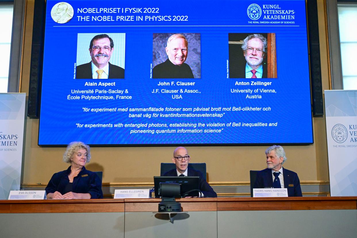 Secretary General of the Royal Swedish Academy of Sciences Hans Ellegren, centre, Eva Olsson, left and Thors Hans Hansson, members of the Nobel Committee for Physics announce the winner of the 2022 Nobel Prize in Physics, from left to right on the screen, Alain Aspect, John F. Clauser and Anton Zeilinger, during a press conference at the Royal Swedish Academy of Sciences, in Stockholm, Sweden, Tuesday, Oct. 4, 2022. 