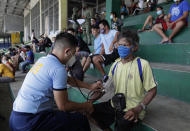 A police officer checks the blood pressure of a man who was apprehended for violating quarantine health protocols at the Amoranto Sports Complex in Manila, Philippines on Wednesday, July 8, 2020. Philippine President Rodrigo Duterte eased one of the world's longest lockdowns in the Philippine capital of more than 13 million people on June 1 after the economy shrank in the first quarter in its first contraction in more than two decades. (AP Photo/Aaron Favila)