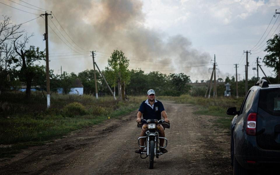 A man rides a motocycle as black smoke rises from the front line in Mykolaiv Oblast -  DIMITAR DILKOFF/AFP