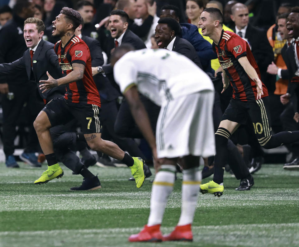 Portland Timbers defender Larrys Mabiala bends over in dejection as Atlanta United forward Josef Martinez (7) and midfielder Miguel Almiron (10) charge the field to celebrate winning the MLS Cup championship soccer game, Saturday, Dec. 8, 2018, in Atlanta. Atlanta won 2-0. (Curtis Compton/Atlanta Journal-Constitution via AP)