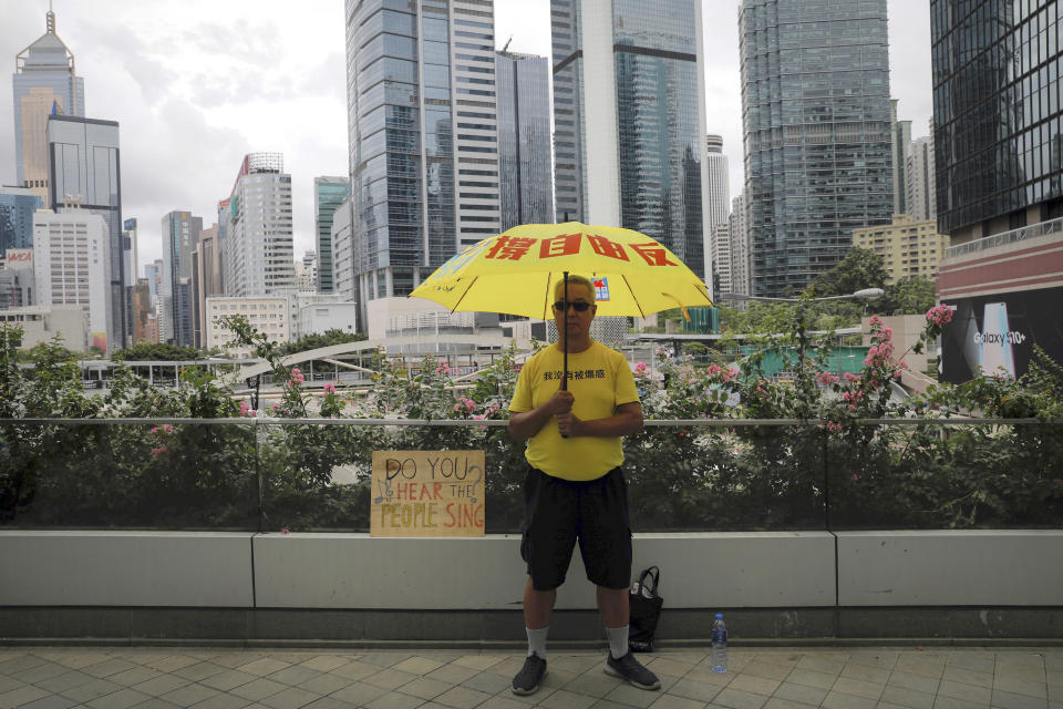 FILE - In this Tuesday, June 18, 2019, file photo, a man holds an umbrella stands outside the Legislative Council following last weekend's massive protest against the unpopular extradition bill in Hong Kong. All but a handful of protesters in Hong Kong have gone home, but the crisis that brought nearly 2 million into the streets to oppose the extradition bill is far from over. (AP Photo/Vincent Yu, File)