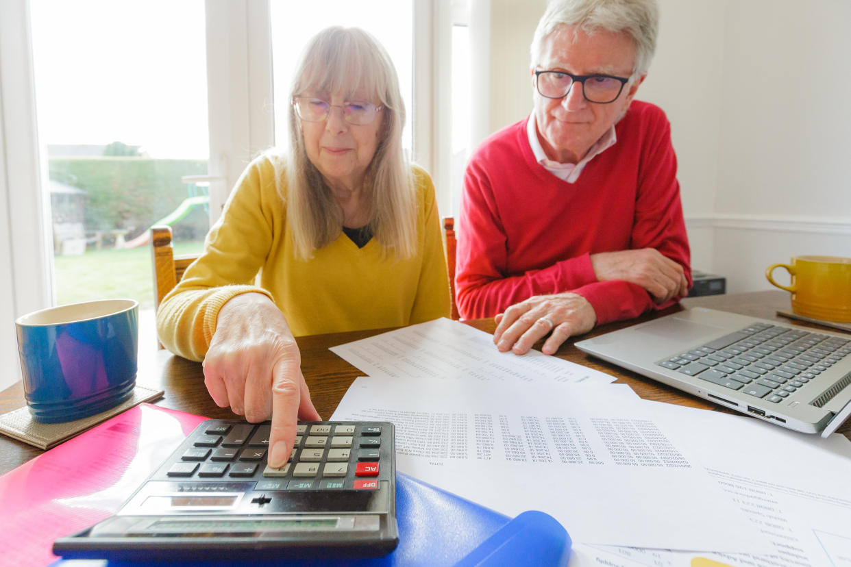 tax A senior couple check their finances at home while surrounded by documents, folders, laptop and a calculator. They both appear slightly worried and anxious.