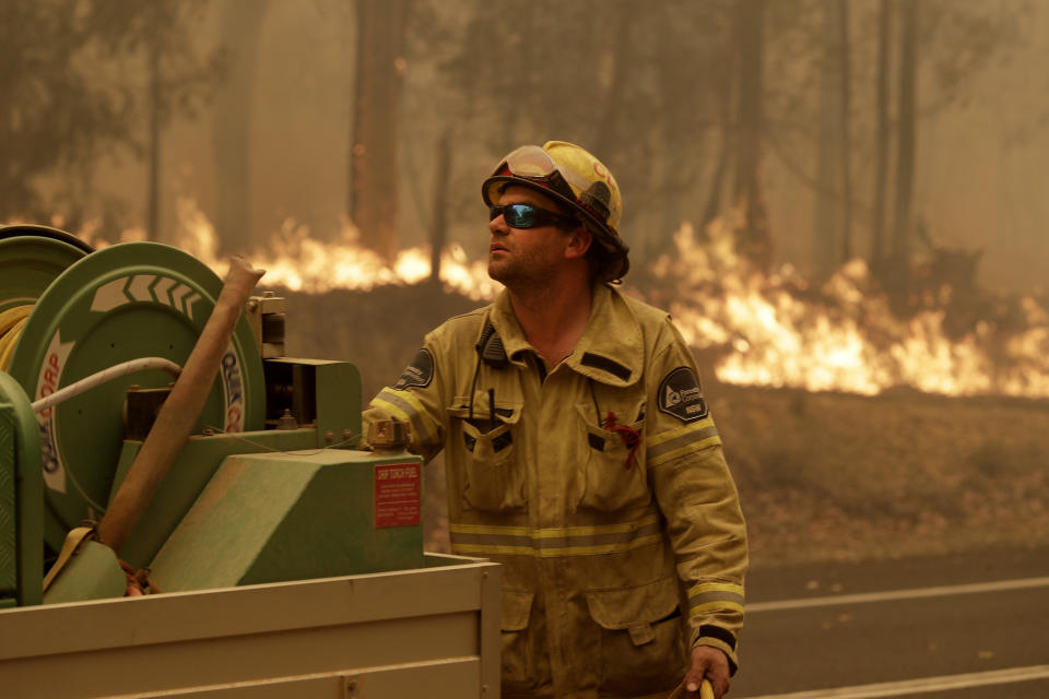 A Forest Corporation worker manages a fire hose as he battles a fire near Moruya, Australia, Saturday, Jan. 4, 2020. Australia's Prime Minister Scott Morrison called up about 3,000 reservists as the threat of wildfires escalated Saturday in at least three states with two more deaths, and strong winds and high temperatures were forecast to bring flames to populated areas including the suburbs of Sydney. (AP Photo/Rick Rycroft)