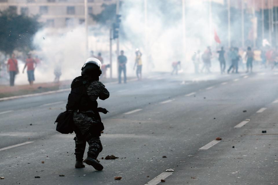 A military police officer fires a tear gas grenade against demonstrators