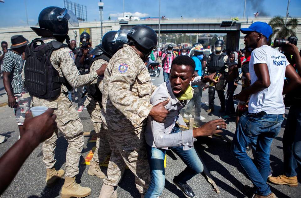 Police officers prevent a protester from fueling a burning barricade during a demonstration demanding the resignation of President Jovenel Moïse, in Port-au-Prince, Haiti, Friday, Jan. 15, 2021.