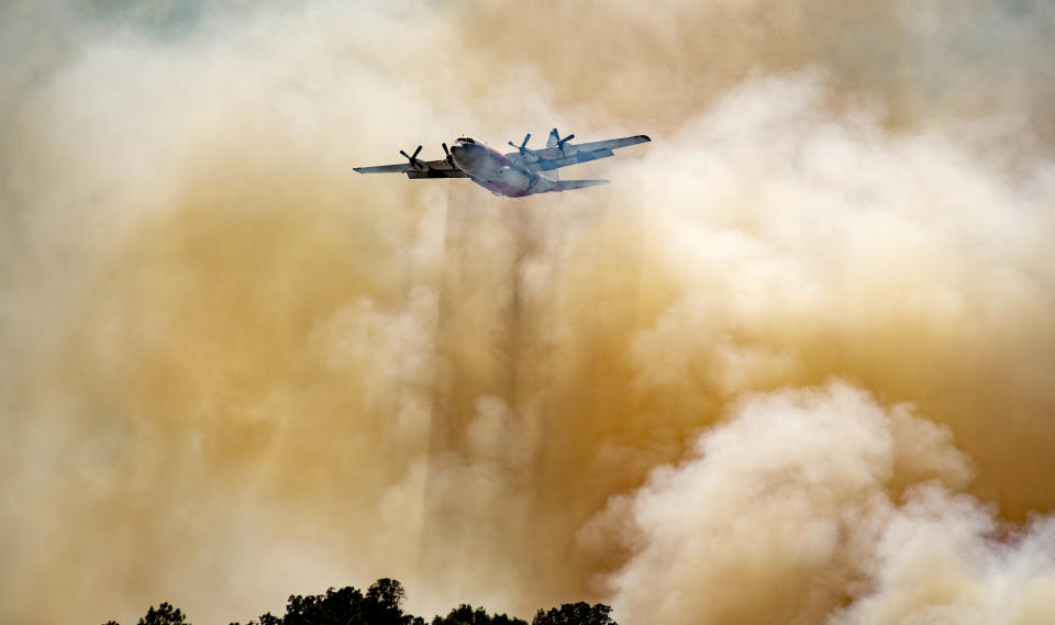 A firefighting aircraft flies through smoke after dropping fire retardant on a hillside in an attempt to box in flames from a wildfire locally called the Sand Fire in Rumsey, Calif., Sunday, June 9, 2019. (AP Photo/Josh Edelson)