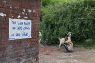 An elderly man sits with his goat at the entrance of Naddi village with a signboard denying entrance to outsiders stuck on a wall in Dharmsala, India, Saturday, June 12, 2021. (AP Photo/Ashwini Bhatia)