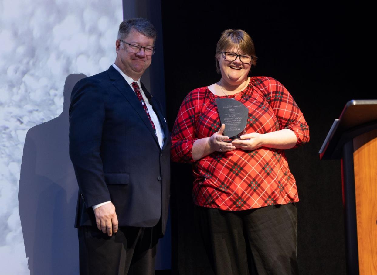 2022 Service Excellence Award Winner Carol Vroman (right) and Reg Smith (left) stand on stage during the Celebration of Champions award ceremony.