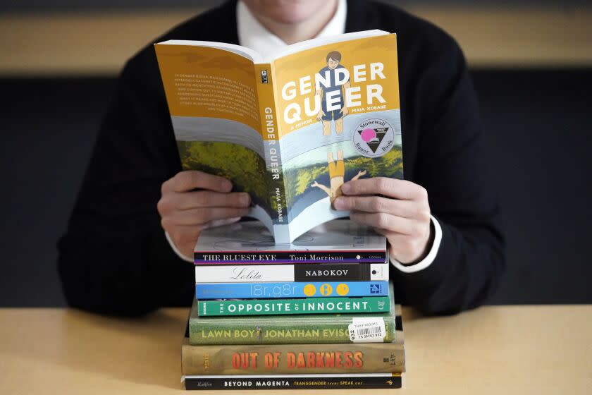 FILE - Amanda Darrow, director of youth, family and education programs at the Utah Pride Center, poses with books that have been the subject of complaints from parents in recent weeks on Thursday, Dec. 16, 2021, in Salt Lake City. A judge in Virginia dismissed a lawsuit Tuesday, Aug. 30, 2022, that sought to declare two books as obscene for children and to restrict their distribution to minors, including by booksellers and libraries. The books in question were "Gender Queer: A Memoir" by Maia Kobabe and "A Court of Mist and Fury" by Sarah J. Maas. (AP Photo/Rick Bowmer)