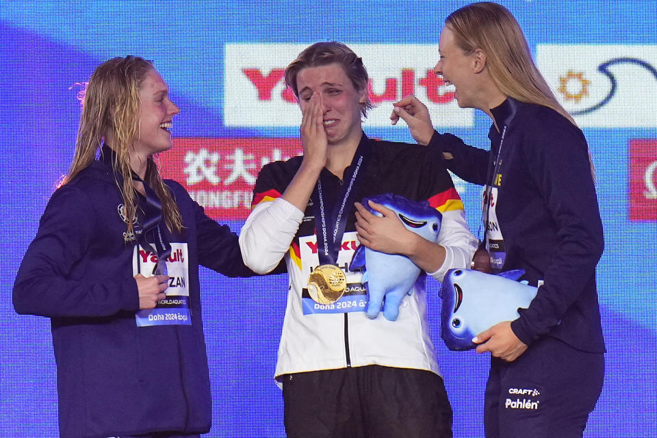 Angelina Kohler of Germany, center, cries at the podium after winning the gold medal in the women's 100m Butterfly Final as she is comforted by Claire Curzan of the United States, left, who won silver, and Louise Hansson of Sweden, who won bronze, at the World Aquatics Championships in Doha, Qatar, Monday, Feb. 12, 2024. (AP Photo/Hassan Ammar)