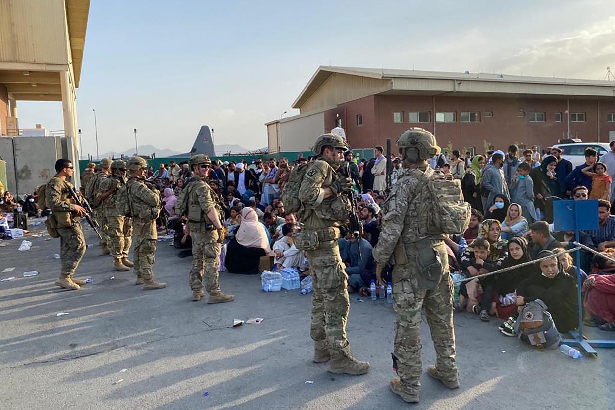 US soldiers stand guard as Afghan people wait to board a US military aircraft  to leave Afghanistan, at the military airport in Kabul on August 19, 2021 after Taliban's military takeover of Afghanistan. (Photo by Shakib RAHMANI / AFP) (Photo by SHAKIB RAHMANI/AFP via Getty Images)