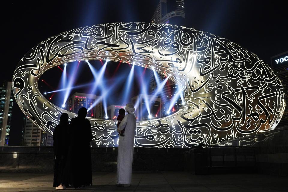 Lights shine down on an Emirati family looking at the under-construction Museum of the Future on National Day in Dubai, United Arab Emirates, Wednesday, Dec. 2, 2020. The UAE is celebrating the 49th anniversary of its founding in 1971 this year. (AP Photo/Jon Gambrell)