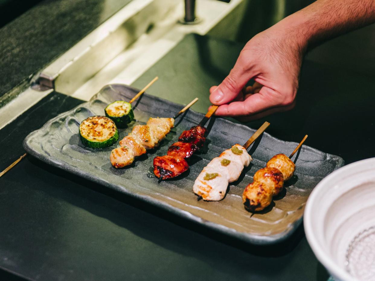 Yakitori (Japanese-Style Grilled Chicken Skewers) with chicken, internal organ and cucumber served on black stone plate with hand pinching.