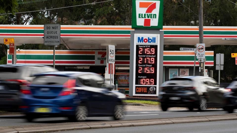 Cars driving past petrol station with sign saying fuel is over $2 a litre.