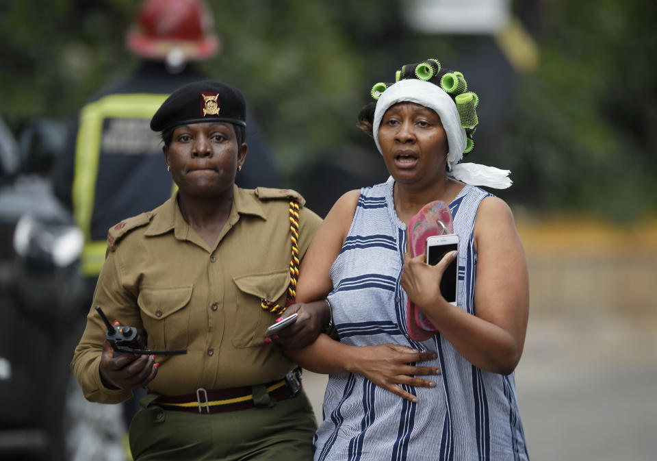 A civilian flees the scene assisted by a member of security forces, at a hotel complex in Nairobi, Kenya Tuesday, Jan. 15, 2019. Terrorists attacked an upscale hotel complex in Kenya's capital Tuesday, sending people fleeing in panic as explosions and heavy gunfire reverberated through the neighborhood. (AP Photo/Ben Curtis)