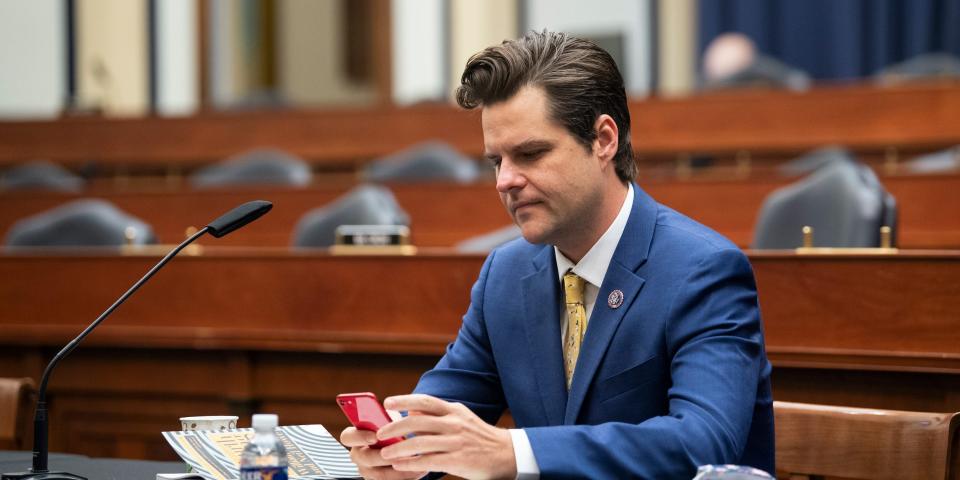 Florida Congressman Matt Gaetz looks at his phone in an empty hearing room.