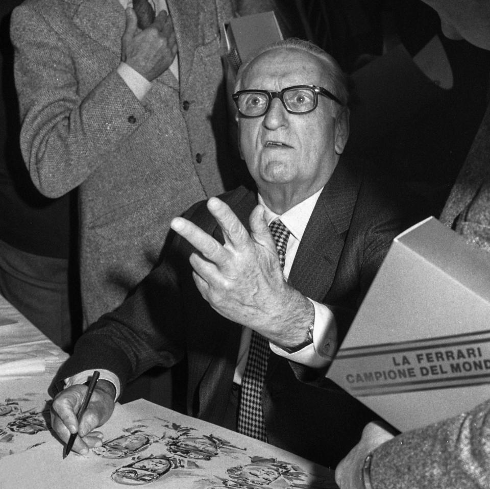 enzo ferrari looking up toward a camera while signing papers with his right hand