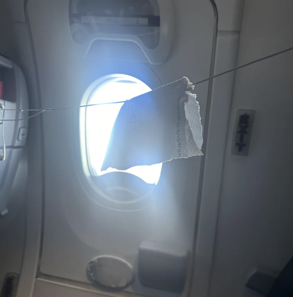 A damaged airplane window with a makeshift patch, bright light shining through