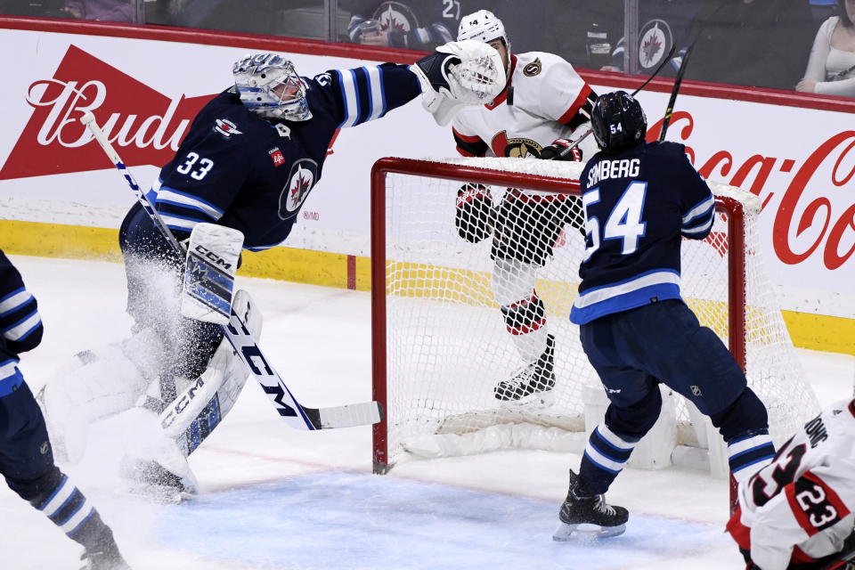 Winnipeg Jets goaltender David Rittich (33) reaches for the puck as Ottawa Senators' Tyler Motte (14) and Jets' Dylan Samberg (54) watch during the first period of an NHL hockey game Tuesday, Dec. 20, 2022, in Winnipeg, Manitoba. (Fred Greenslade/The Canadian Press via AP)
