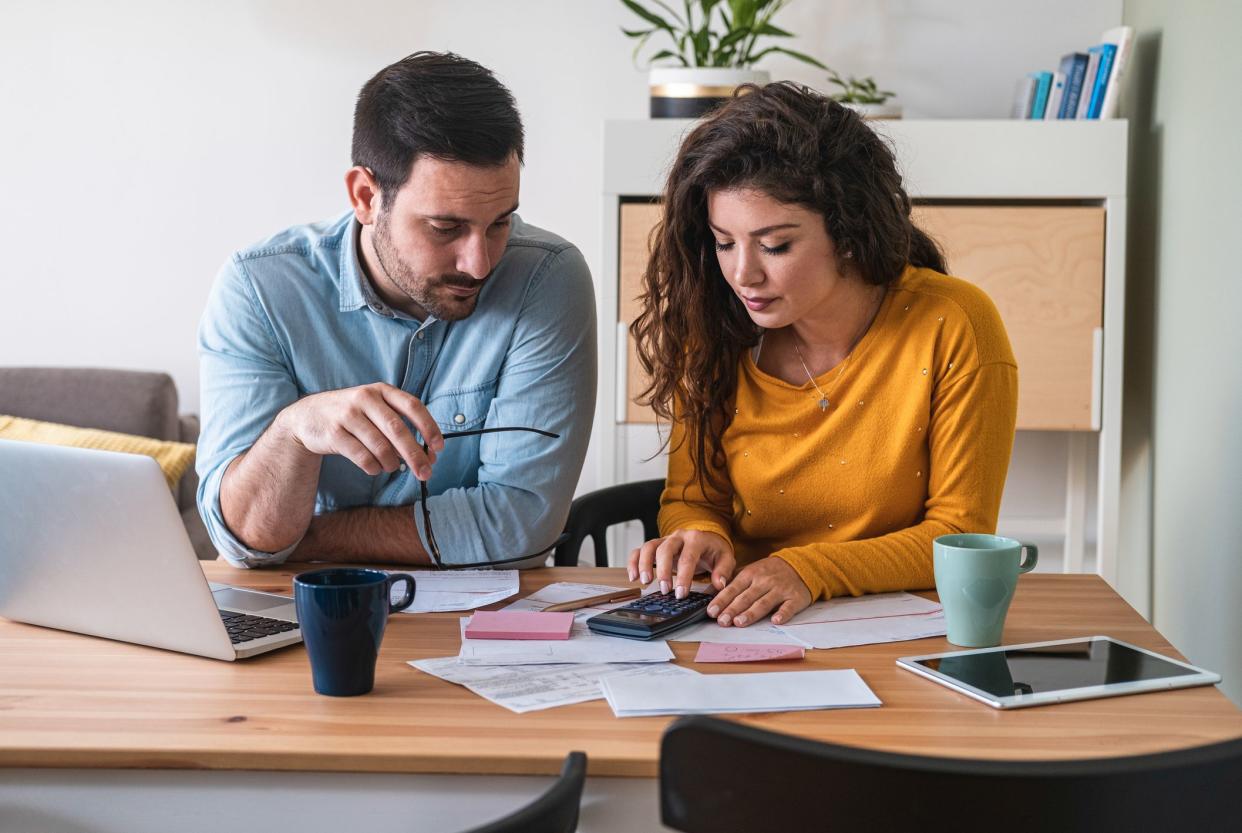 Focused married couple manage finances, use internet banking service on computer and calculator at modern kitchen desk