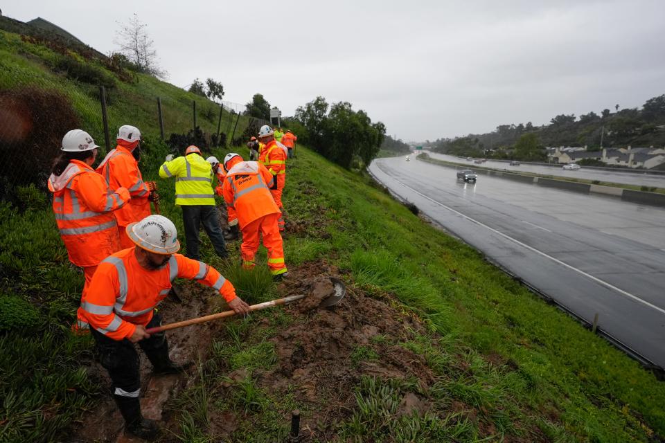 Caltrans workers clear debris from a canal to keep a hillside from flooding during a rain storm Thursday, Feb. 1, 2024, in San Diego. Heavy rain and gusty winds began hitting the north on Wednesday and moved south along the coast, snarling the Thursday morning commute in Southern California.
