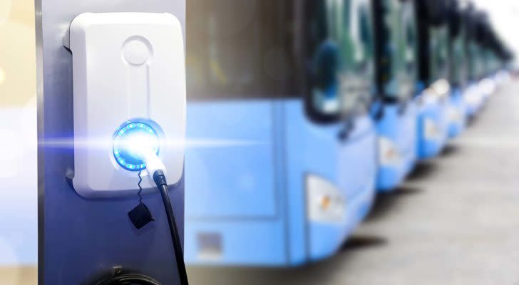 A close-up shot of an electric vehicle charging station with a row of electric buses in the background.