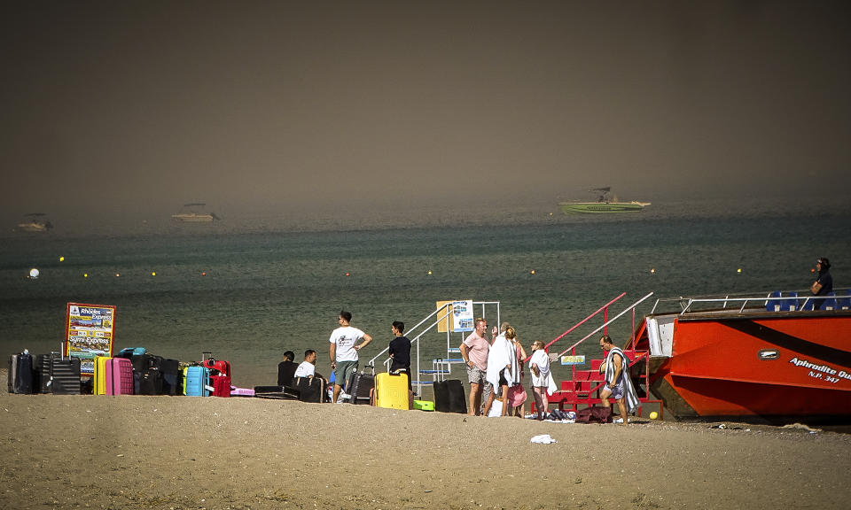 Tourists stand on a beach after being evacuated during a forest fire on the island of Rhodes, Greece, Saturday, July 22, 2023. A large blaze burning on the Greek island of Rhodes for the fifth day has forced authorities to order an evacuation of four locations, including two seaside resorts. (Argyris Mantikos/Eurokinissi via AP)