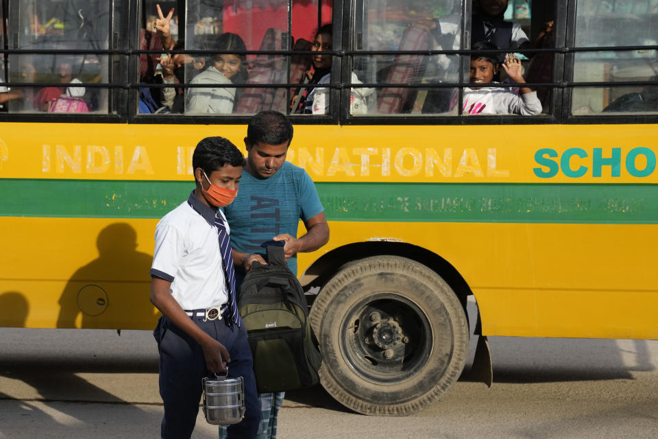 Raju, left, meets his father Jaidul Islam after his school bus dropped him near his home in a poor neighborhood in Bengaluru, India, Tuesday, July 19, 2022. A flood in 2019 in the Darrang district of India's Assam state started Raju, his sister Jerifa and their parents on a journey that led the family from their Himalayan village to the poor neighborhood. (AP Photo/Aijaz Rahi)