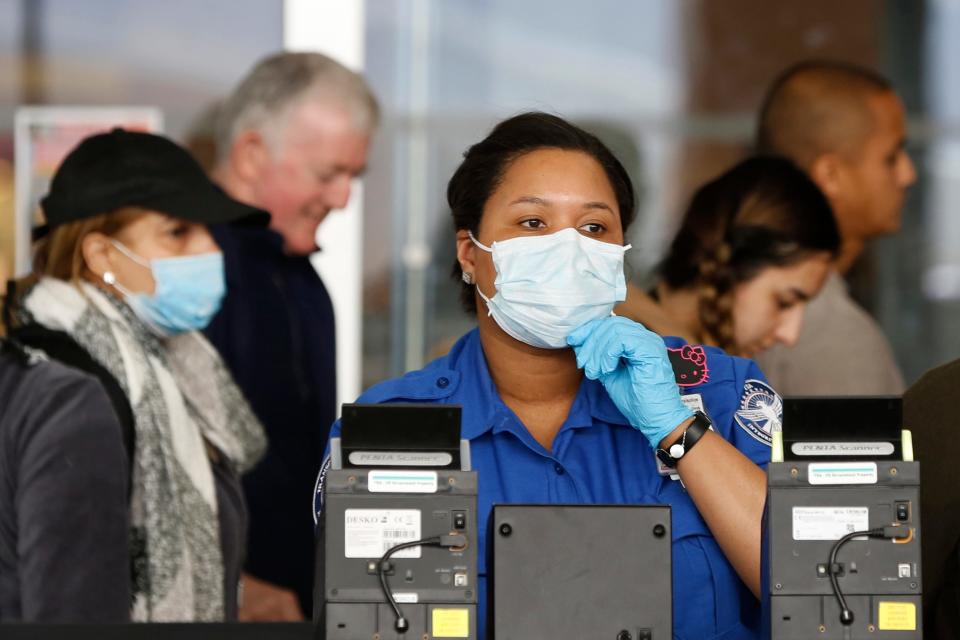 A Transportation Security Administration (TSA) employee adjusts her face mask while screening passengers entering through a checkpoint at John F. Kennedy International Airport, Saturday, March 14, 2020, in New York.