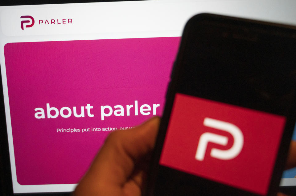 The logo of the social media platform Parler is displayed in Berlin, Jan. 10, 2021. In the background on a screen is the platform's website. The conservative-friendly social network Parler was booted off the internet Monday, Jan. 11, over ties to last week's siege on the U.S. Capitol, but not before hackers made off with an archive of its posts, including any that might have helped organize or document the riot. (Christophe Gateau/dpa via AP)