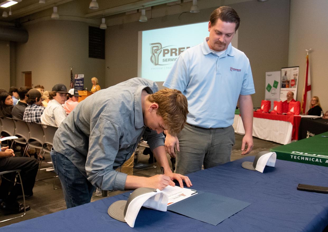 May 11, 2022; Tuscaloosa, AL, USA; Cameron Scott signs his employment certificate under the watchful eye of Premier Service Company’s Kyle Chronister at the Tuscaloosa Career and Technology Academy Signing Day Wednesday. TCTA prepares students with a technical education in preparation for graduates entering the work force. Signing day gives the students an opportunity to sign employment or apprenticeship agreements with local employers. Gary Cosby Jr.-The Tuscaloosa News