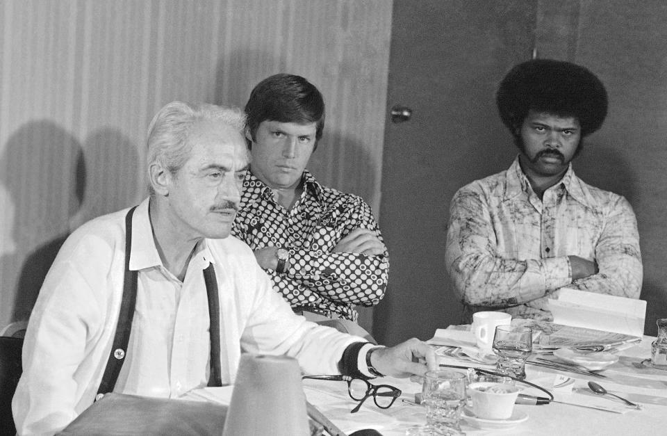 FILE - In this Saturday, March 13, 1976, file photo, Marvin Miller, executive director of the baseball players association, holds a news conference in St. Petersburg, Fla., as New York Mets pitcher Tom Seaver, rear left, and St. Louis Cardinals' Reggie Smith look on. The 1970s. Players of color finally stepping into an unfettered spotlight, the reserve clause ending, free agency beginning and the players’ union finding its voice. (AP Photo/File)