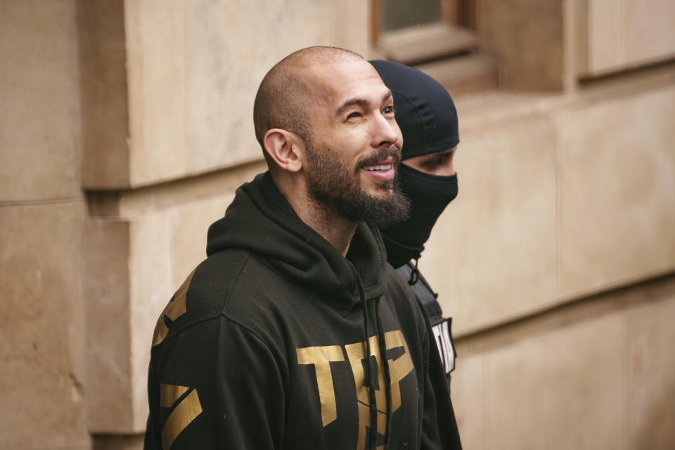 A police officer escorts Andrew Tate, center, handcuffed, from the Court of Appeal in Bucharest, Romania, Tuesday, March 12, 2024. Online influencer Andrew Tate was detained in Romania and handed an arrest warrant issued by British authorities, his spokesperson said Tuesday. (AP Photo/Andreea Alexandru)