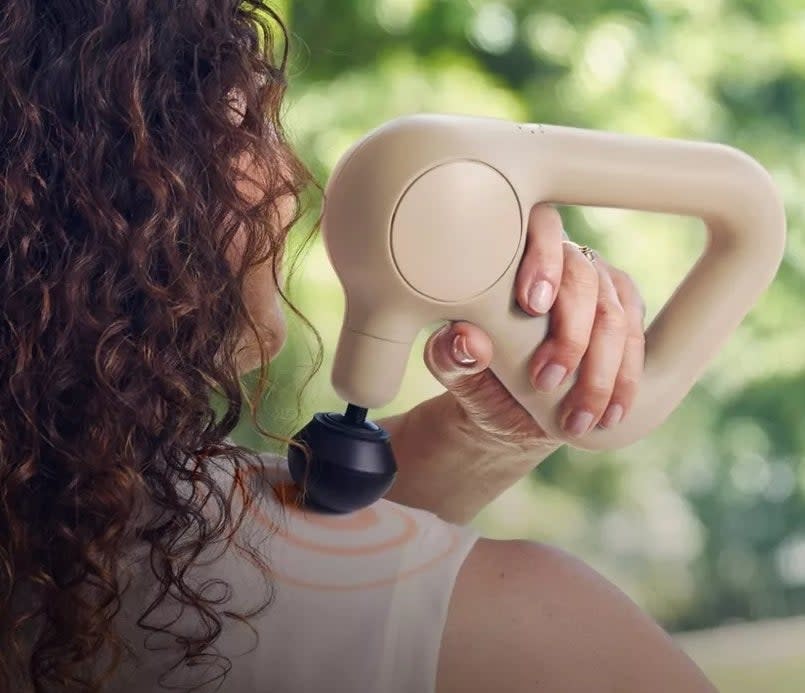 Person using a handheld massaging device on their shoulder to relieve muscle tension