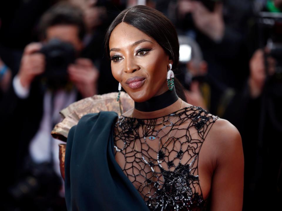 Naomi posing in a black sheer lace dress on a red carpet.