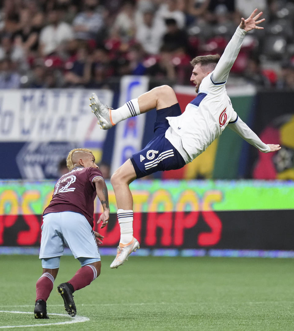 Vancouver Whitecaps' Tristan Blackmon (6) falls over Colorado Rapids' Michael Barrios (12) as they vied for the ball during the second half of an MLS soccer match Wednesday, Aug. 17, 2022, in Vancouver, British Columbia. (Darryl Dyck/The Canadian Press via AP)