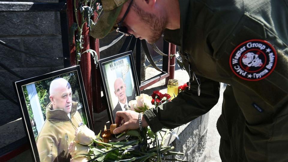 PHOTO: TOPSHOT - A member of private mercenary group Wagner pays tribute to Yevgeny Prigozhin (L) and Dmitry Utkin at the makeshift memorial in front of the PMC Wagner office in Novosibirsk, on August 24, 2023. (Vladimir Nikolayev/AFP via Getty Images)