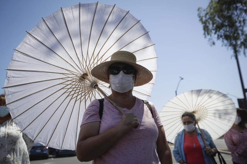 The faithful use face masks and parasols during an outdoor prayer amid the coronavirus pandemic at the San Gabriel Mission, Sunday, July 12, 2020, in San Gabriel, Calif. A fire on Saturday destroyed the rooftop and most of the interior of the nearly 250-year-old California church that was undergoing renovation. (AP Photo/Marcio Jose Sanchez)