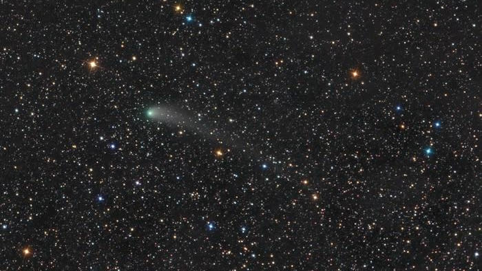  The black of space is filled with stars of varying size and brightness. near the center, a larger green star is actually a comet and has a faint green tail to the right. 