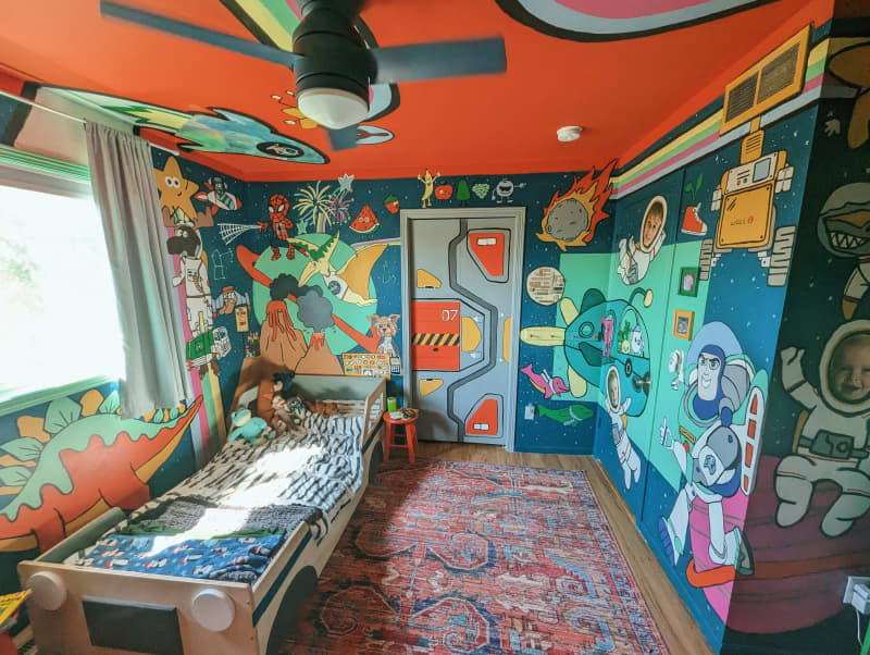 kids room with colorful space and dinosaur themed painted walls and ceiling