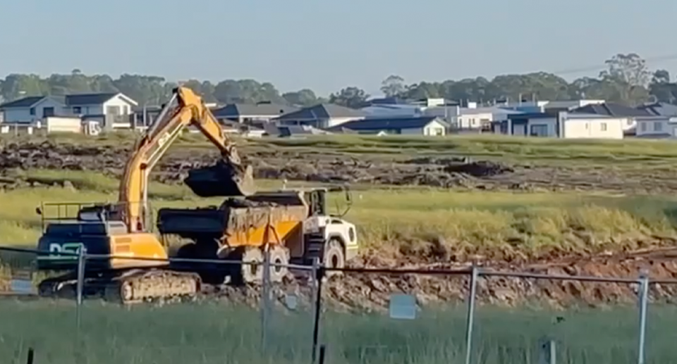 Large construction vehicles can be seen digging mud out of the dam. 