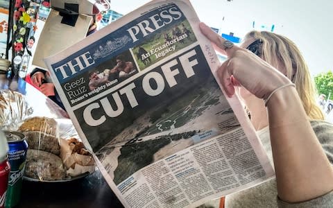 A  tourist reads a local newspaper with a headline about the storms hitting New Zealand's South Island - Credit: DAVID GRAY/AFP/GETTY IMAGES
