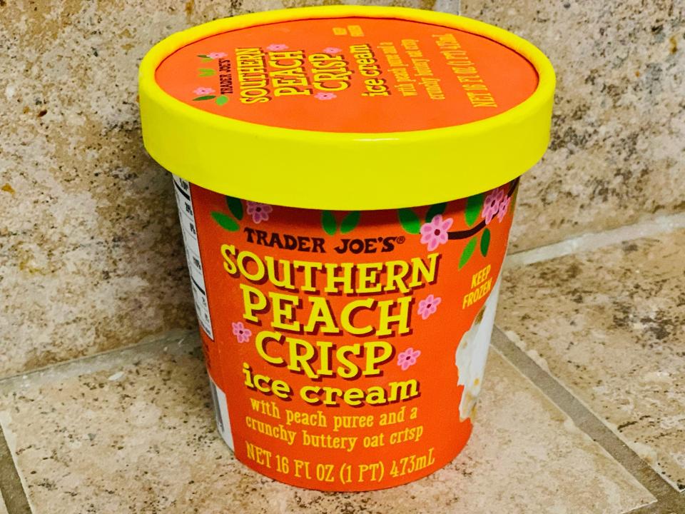 Trader joe's southern peach crisp ice cream in the original orange and yellow packaging against beige tile