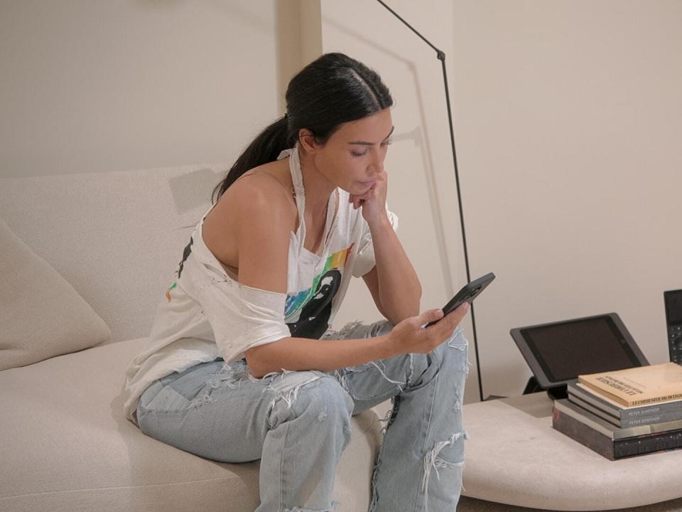 kim kardashian sitting on a couch, looking down at her phone with concern