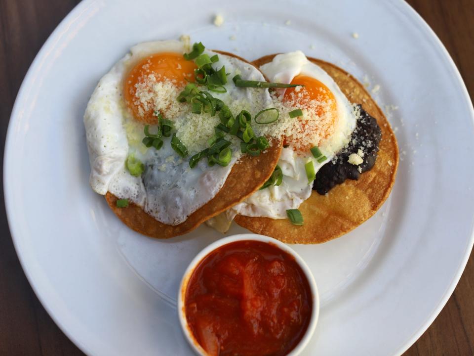 two sunny side up eggs on tortillas with black beans and a side of red sauce; huevos rancheros