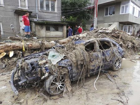 People inspect debris behind a car destroyed by heavy floods in Varna June 21, 2014. REUTERS/Impact Press Group